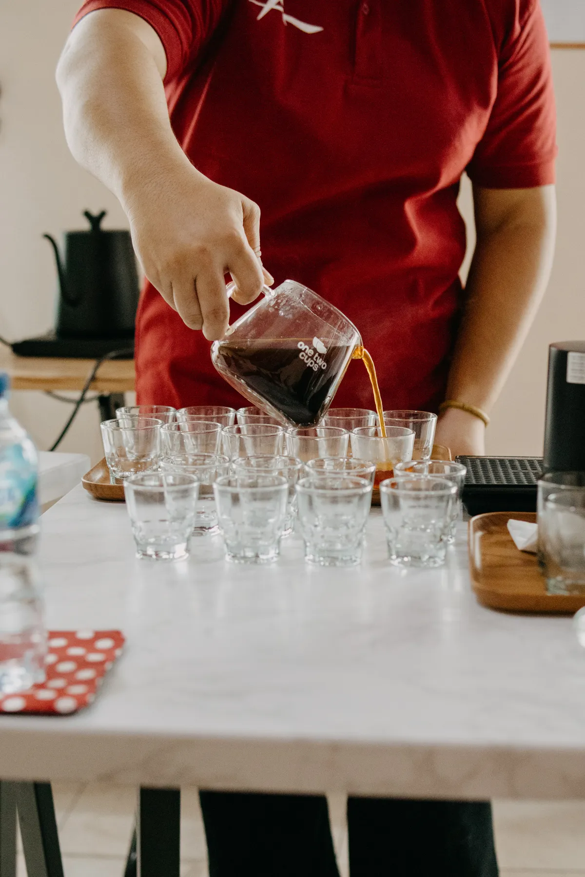 A team member pouring brewed coffee into tasting cups during a cupping session