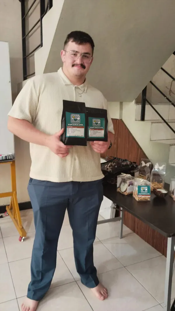 A member of the Kopi Suka Cita team holding two bags of roasted coffee